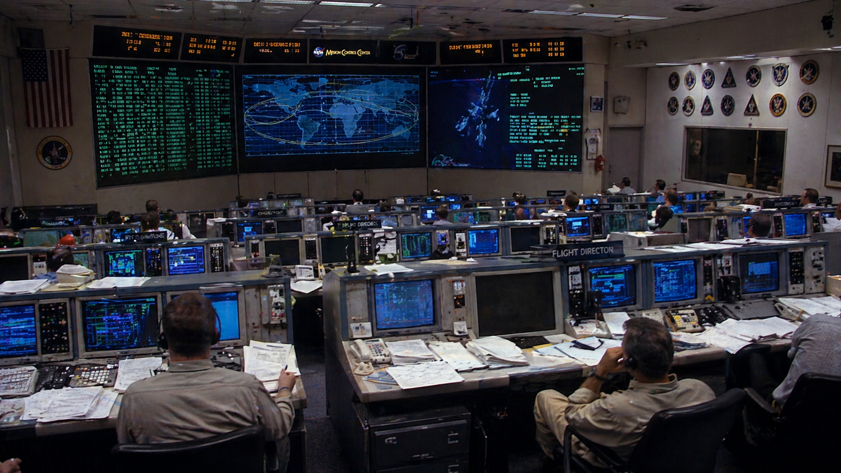 NASA Mission Control room — vintage workstations, monitors, and Earth orbital tracking display